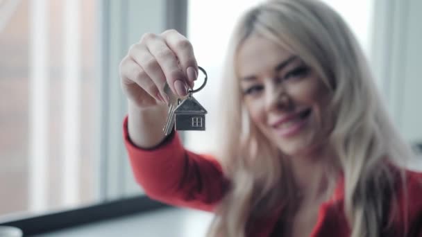 Mortgage concept. Woman in red business suit holding key with house shaped keychain. Modern light lobby interior. Real estate, moving home or renting property. — Stock Video