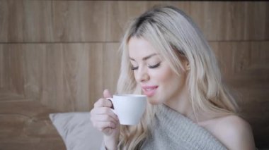 Seramik fincan çay ya da kahve tutan güzel sarışın kadın tadını çıkarın. Yatak odasında çay saati. Pencere ve içecek çay arıyorum. Günaydın. Pretty genç kız rahatlatıcı. Mutlu kış konsepti