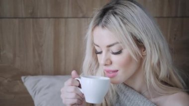 Seramik fincan çay ya da kahve tutan güzel sarışın kadın tadını çıkarın. Yatak odasında çay saati. Pencere ve içecek çay arıyorum. Günaydın. Pretty genç kız rahatlatıcı. Mutlu kış konsepti.