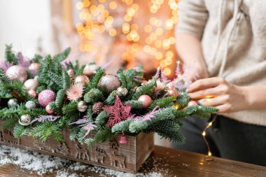 Genç kadın oluşturur ve taze Ladin, süsbitkileri bir rustik ahşap kutu kutu içinde güzel Festival düzenleme süsler. Noel ruh. Garland bokeh arka plan üzerinde.