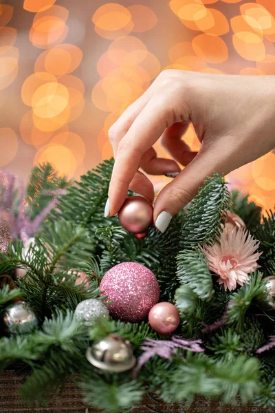 Jonge vrouw wordt gemaakt en mooie feestelijke regeling van verse spar, siergewassen in een rustieke houten vak siert. Kerstsfeer. Garland bokeh op achtergrond. — Stockfoto