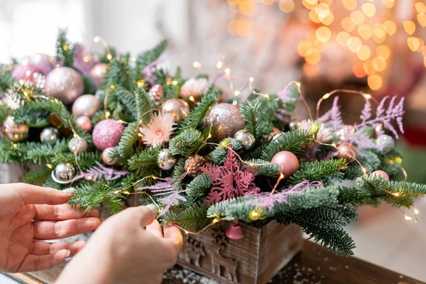 Giovane donna crea e decora bella disposizione festiva di abete rosso fresco, ornamentali in una scatola di legno rustico. L'umore natalizio. Ghirlanda bokeh sullo sfondo . — Foto Stock