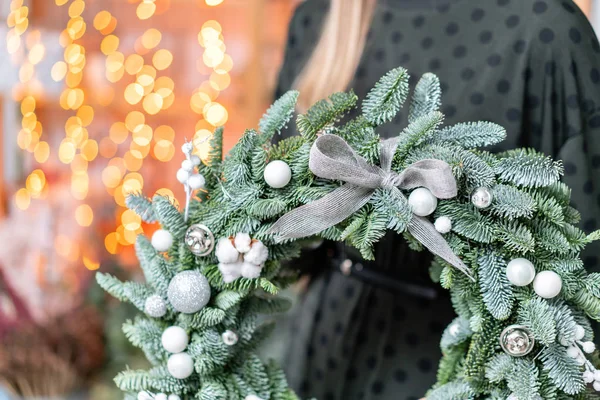 Compras de Natal. Grinalda de Natal verde em mãos femininas. Decorado com elementos cinza, algodão e bola de prata. Garland bokeh em segundo plano . — Fotografia de Stock