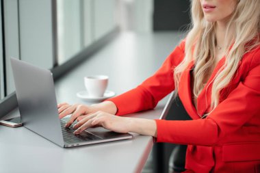 Kırmızı mercan iş takım elbiseli kadın. Sarışın genç iş kadını ile modern gri laptop pencerenin önünde yüksek kat ofisinde. Kahve içme kız