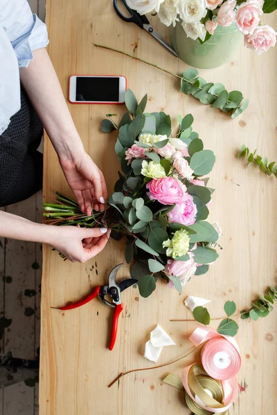 El profesyonel çiçekçi bir buket pembe Düğünçiçeği ve peonies bir çiçekçide yapma Close-up. Düzenleme ve buket ambalaj. Kavram çiçek satışı ve online mağaza