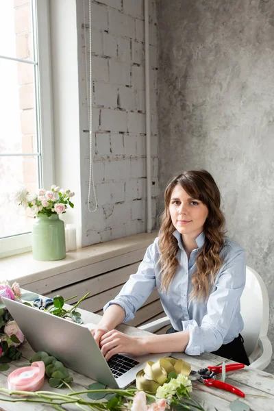 Genç dostu gülümseyen kadın çiçekçi oluşturmak bir dizüstü bilgisayarda temel çalışma sipariş. Çiçek teslimat kavramı. Bir çiçekçi dükkanı profesyonel işçi.