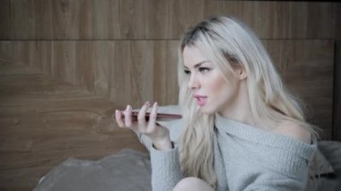 Yatakta oturmuş ve onun elleri ile telefonda konuşmak rüya gibi güzel sarışın kadın. Akıllı robot yardımcı modern telefonlarda'kavramı. Blogging, internet tarama, sohbet.
