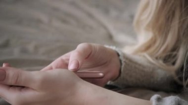 Güzel sarışın kadın ile akıllı telefon yatakta yatıyordu. Kız gülümsüyor, iyi bir ruh hali. Blogging, internet tarama, sohbet. Sıcak sıcak kazak ve yün çorap. Mutlu kış konsepti.