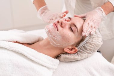 Doktor hasta yüzünden jel kaldırır ve terapötik bir krem uygulayın. Anti akne fototerapi. Güzel kadın fotoğraf gençleştirme işlemi sırasında. Yüz cilt bakımı kozmetik kliniğinde.