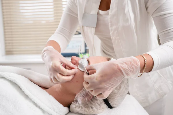 O médico coloca os óculos do paciente. Fototerapia anti acne com equipamento profissional. Mulher bonita no salão de beleza durante o procedimento de rejuvenescimento de fotos. Tratamento da pele da cara na clínica cosmética . — Fotografia de Stock