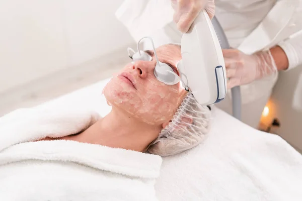 Fototerapia anti acne com equipamento profissional. Mulher bonita no salão de beleza durante o procedimento de rejuvenescimento de fotos. Tratamento da pele do rosto do laser na clínica cosmética. Cosmetologia de hardware — Fotografia de Stock