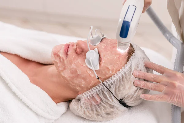 Fototerapia anti acne com equipamento profissional. Mulher bonita no salão de beleza durante o procedimento de rejuvenescimento de fotos. Tratamento da pele do rosto do laser na clínica cosmética. Cosmetologia de hardware — Fotografia de Stock