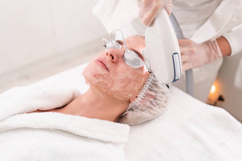 Anti acne phototherapy with professional equipment. Beautiful woman in beauty salon during photo rejuvenation procedure. Laser face skin treatment at cosmetic clinic. Hardware cosmetology