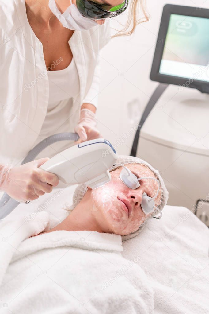 Anti acne phototherapy with professional equipment. Beautiful woman in beauty salon during photo rejuvenation procedure. Laser face skin treatment at cosmetic clinic. Hardware cosmetology