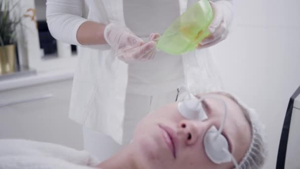 El médico aplica un gel especial al paciente. Fototerapia anti acné con equipo profesional. Hermosa mujer durante el procedimiento de rejuvenecimiento de fotos. Tratamiento de la piel de la cara en clínica cosmética . — Vídeo de stock