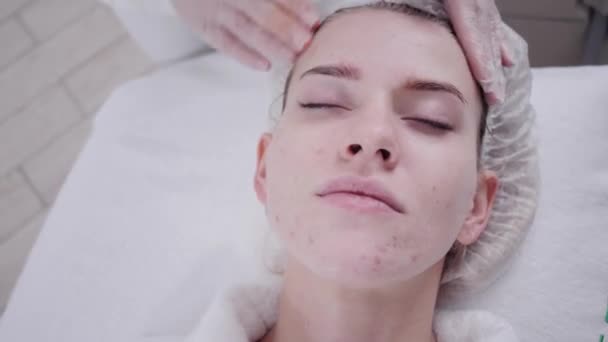 The doctor removes the gel from the patients face and apply a therapeutic cream. Anti acne phototherapy. Beautiful woman during photo rejuvenation procedure. Face skin treatment at cosmetic clinic. — Stock Video