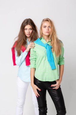 mutlu kız kadın gömlek ve bir kazak onun omuzlarında. İki kız kardeş moda bahar görüntüsü. Renkler renkli kıyafetler. Modelleri ile sarışın ve ışık kahverengi saç. Kameraya bakarak ve gülümseyen.