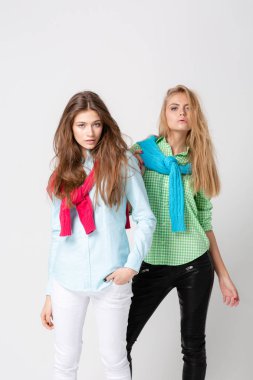 mutlu kız kadın gömlek ve bir kazak onun omuzlarında. İki kız kardeş moda bahar görüntüsü. Renkler renkli kıyafetler. Modelleri ile sarışın ve ışık kahverengi saç. Kameraya bakarak ve gülümseyen.