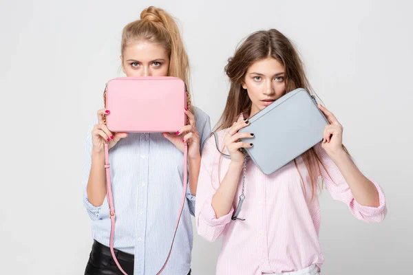 Freundinnen in Hemden mit stylischen Handtaschen. Mode Frühjahr Bild von zwei Schwestern. Pastellrosa und blauen Farben Kleidung. Models mit blonden und hellbraunen Haaren. — Stockfoto