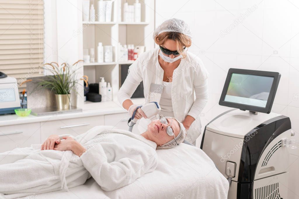 The doctor applies a special gel to the patient. Anti acne phototherapy with professional equipment. Beautiful woman during photo rejuvenation procedure. Face skin treatment at cosmetic clinic.