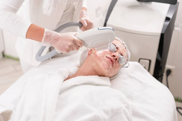 Fototerapia anti acne com equipamento profissional. Mulher bonita no salão de beleza durante o procedimento de rejuvenescimento de fotos. Tratamento da pele do rosto do laser na clínica cosmética. Cosmetologia de hardware — Fotografia de Stock