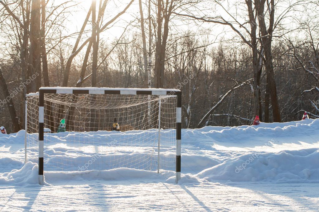 Empty football gate on the field powdered by snow. Dawn frosty morning. Winter landscape of frosty trees, white snow and blue sky. Tranquil winter nature in sunlight in park