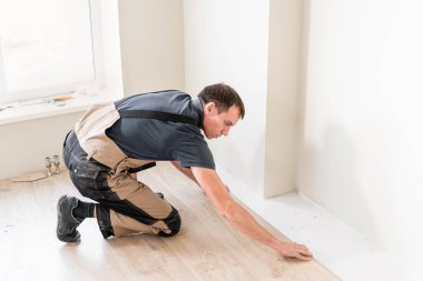 Erkek işçi yeni ahşap laminat parke yükleme. Laminat ve seramik döşeme bal peteği şeklinde ahşap paneller birleşimi. Mutfak yenileme