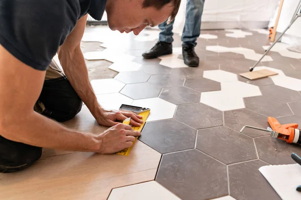 Male worker installing new wooden laminate flooring. The combination of wood panels of laminate and ceramic tiles in the form of honeycomb. Kitchen renovation — Stock Photo, Image
