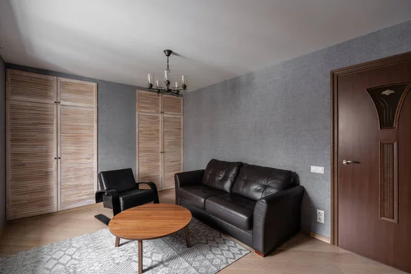 Rusia, Nizhny Novgorod - 10 de enero de 2018: Apartamento privado. Salón moderno con sofá de cuero, sillón, mesa de centro de madera. almohadas en acogedor sofá y lámparas. Diseño de interiores — Foto de Stock