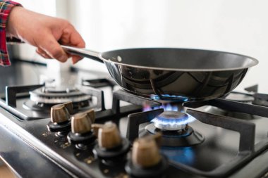 Bir adam bir tavada aşçılar ocakta koyar. Modern gaz yakıcı ve hob bir mutfak grubu hakkında. Koyu siyah renkli ve modern bir dairede ahşap küçük mutfak