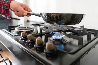 Bir adam bir tavada aşçılar ocakta koyar. Modern gaz yakıcı ve hob bir mutfak grubu hakkında. Koyu siyah renkli ve modern bir dairede ahşap küçük mutfak