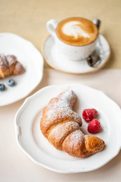 Kaffe cappuccino med två croissant på vit platta i restaurangen. Ljus morgon frukost, färska varma bakverk och hallon — Stockfoto