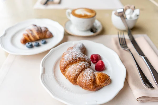 Koffie cappuccino met twee croissant op witte plaat in restaurant. Lichte ochtend ontbijt, verse warme broodjes en frambozen — Stockfoto