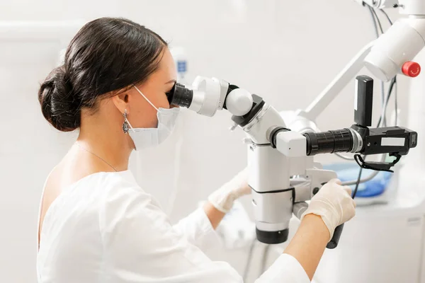 Dentista mulher usuário avançado, ferramentas dentárias. Olhando para a lente de um microscópio enquanto examina os dentes de seus pacientes. no consultório odontológico. Conceito de medicina, odontologia e cuidados de saúde . — Fotografia de Stock