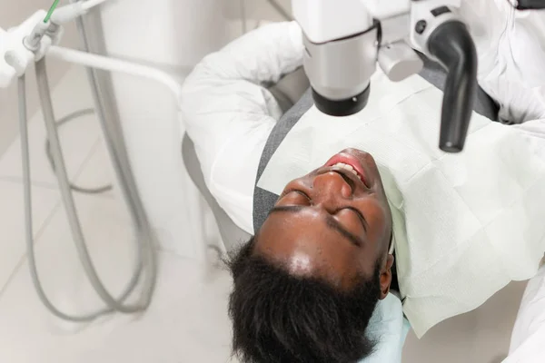 Joven paciente afroamericano en silla en la clínica dental. Medicina, salud, concepto estomatológico. dentista realiza inspección y concluye — Foto de Stock