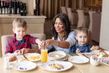 Bebek oğulları olan güzel kadın. Pencere bir kafede yakınındaki hafif kahvaltı. Ay çöreği, omlet, kahve ve birçok farklı yemekler kafede masada. Mutlu bir aile
