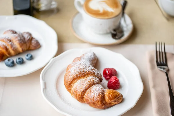 Café capuchino con croissant en plato blanco en restaurante. Desayuno ligero por la mañana, pasteles calientes frescos y frambuesas — Foto de Stock