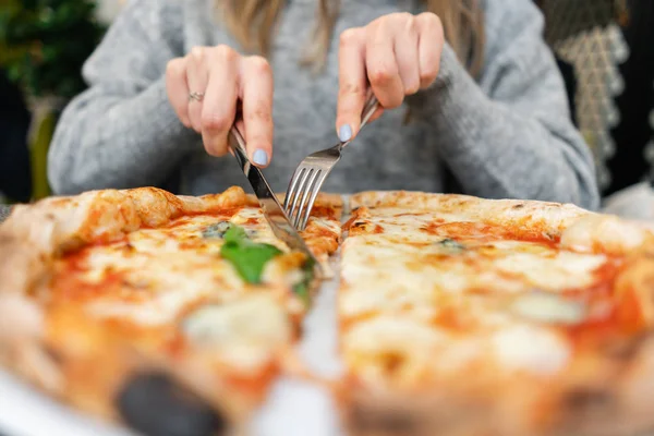 Frau isst mit Messer und Gabel eine Pizza Margherita mit Mozzarella-Tomaten und Basilikum. neapolitanische Pizza aus dem Holzofen. Mittagessen in einem italienischen Restaurant. Tisch neben einem großen Fenster. — Stockfoto