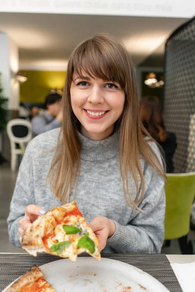 A woman is eating Neapolitan pizza from wood-burning stove. lunch in an Italian restaurant. Table near to a large window. Margarita and four cheese — Stock Photo, Image