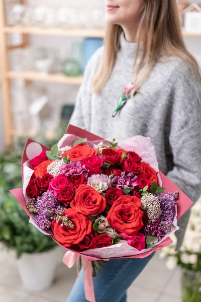 Hermoso ramo fresco cortado de flores mixtas en mano de mujer. el trabajo de la floristería en una florería. Color rojo — Foto de Stock