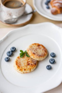 Peynirli kek, taze yaban mersini ve kapuçino. Süzme peynir krep veya lor beyaz tabakta börek. Gündoğumu sağlıklı ve diyet kahvaltı