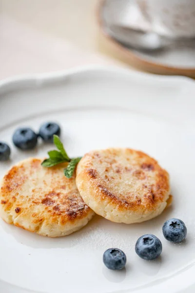 Cheesecake, mirtillo fresco e cappuccino. Frittelle di fiocchi di latte o frittelle di cagliata su piatto bianco. Colazione sana e dietetica all'alba — Foto Stock