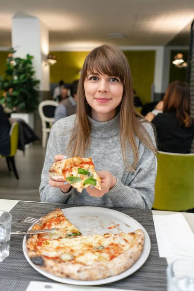 A woman is eating Neapolitan pizza from wood-burning stove. lunch in an Italian restaurant. Table near to a large window. Margarita and four cheese — Stock Photo, Image