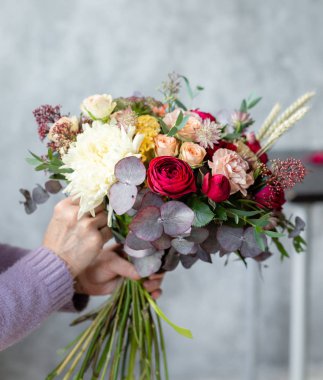 Yakın çekim elinde çiçekler. Çiçekçi işyeri. Kadın bir buket gül, kasımpatı, karanfil ve diğer çiçekleri ile düzenlenmesi. Floristik ana sınıfları veya dersleri öğretmeni