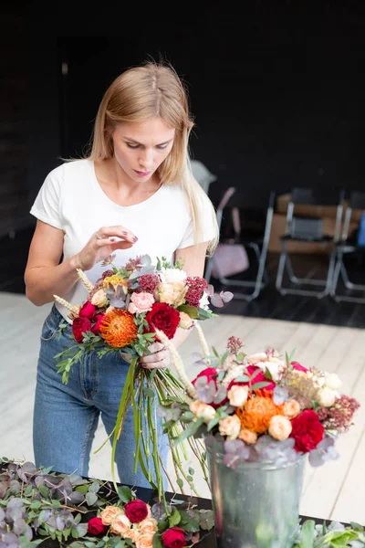Floristik-Arbeitsplatz. Frau arrangiert einen Strauß mit Rosen, Chrysanthemen, Nelken und anderen Blumen. ein Floristikstudent in Meisterkursen oder Kursen — Stockfoto