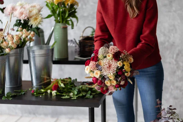 Close-up flowers in hand. Florist workplace. Woman arranging a bouquet with roses, chrysanthemum, carnation and other flowers. A teacher of floristry in master classes or courses