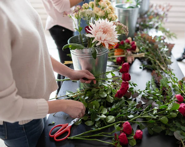 Flores de cerca en la mano. Trabajo florista. Mujer arreglando un ramo con rosas, crisantemo, clavel y otras flores. Un profesor de floristería en clases magistrales o cursos — Foto de Stock