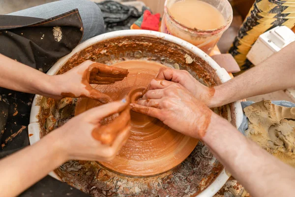 Ceramista mestre ensina estudante.Ceramista mestre ensina estudante. Mãos de artesão fazendo tigela de cerâmica. Mulher a trabalhar na roda de oleiro. Família loja de negócios esculpe pote de argila vista topo. — Fotografia de Stock