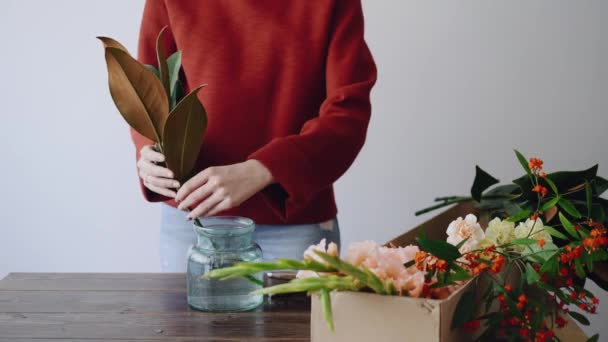 女性の花屋は、ガラスの花瓶と新しいフラワーアレンジメントを作るの花を置きます。女性ボックスから新鮮な花を摘んで花瓶に美しい花束を作成します。フラワー ショップ コンセプト — ストック動画