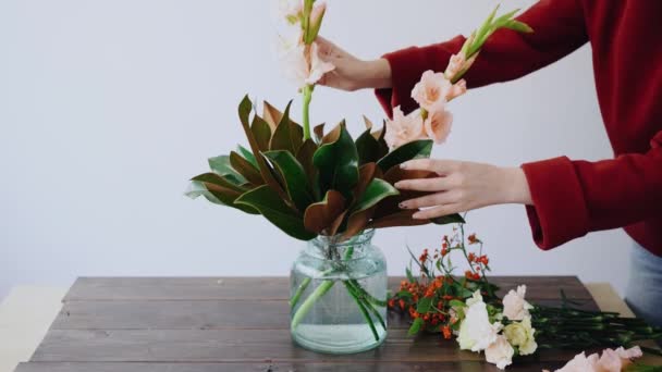 女性の花屋は、ガラスの花瓶と新しいフラワーアレンジメントを作るの花を置きます。女性ボックスから新鮮な花を摘んで花瓶に美しい花束を作成します。フラワー ショップ コンセプト — ストック動画